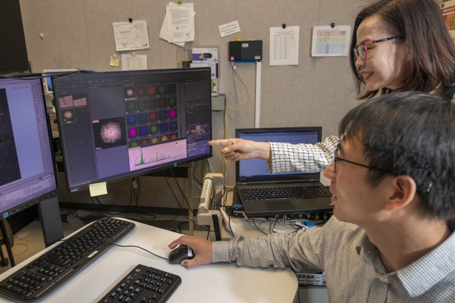 Two researchers point left toward a monitor setup.