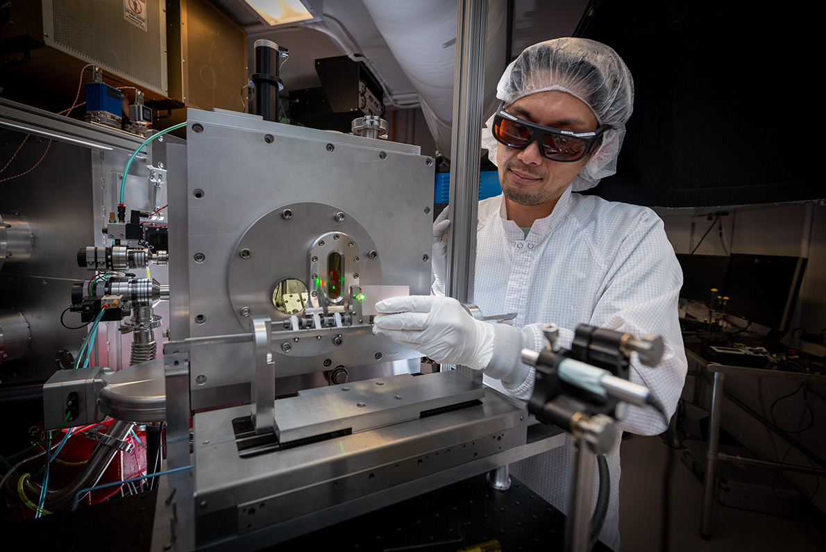 Scientist in protective gear adjusts scientific instrumentation.