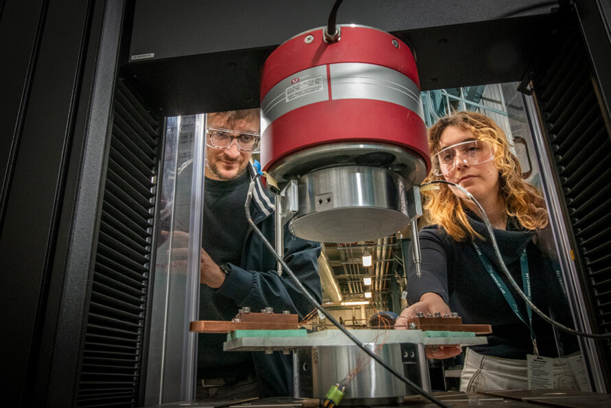 Two researchers in protective glasses look into a superconducting magnet experimental setup.