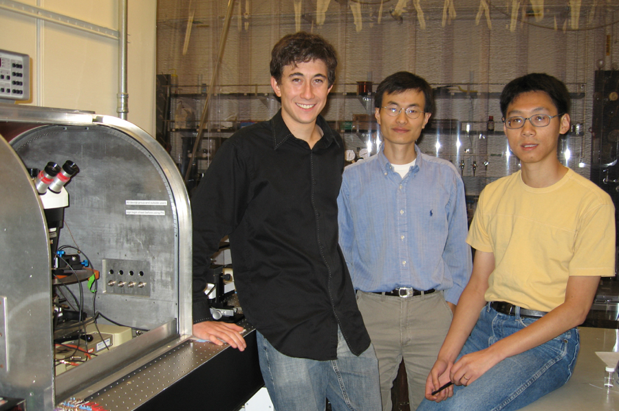 Three researchers posed in a science laboratory There is a microscope on the left side.