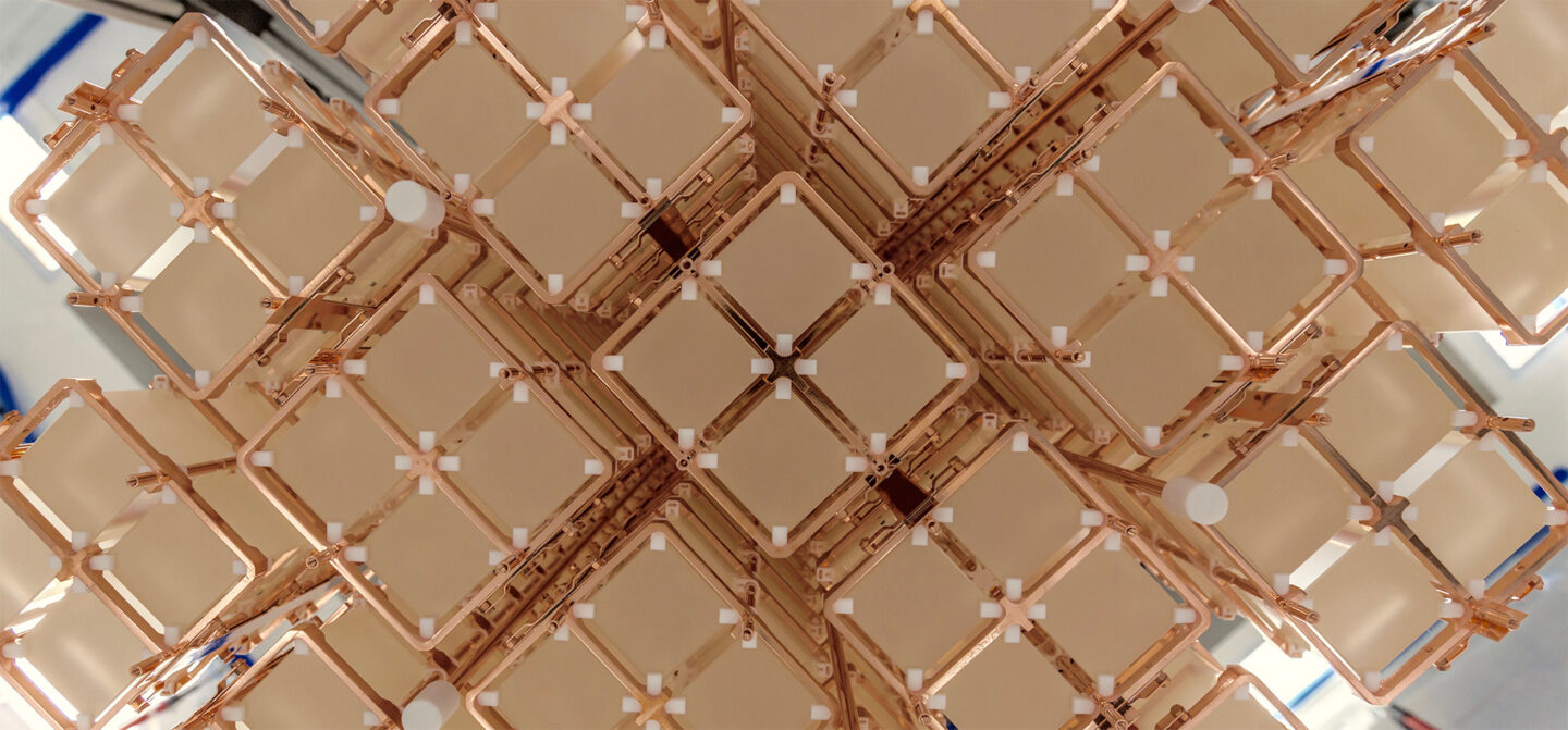 Close-up view of an array of cubic, pale crystals held in a copper framework. The structure is composed of multiple repeating units arranged in a symmetrical, grid-like pattern, with small white spacers at the intersections.