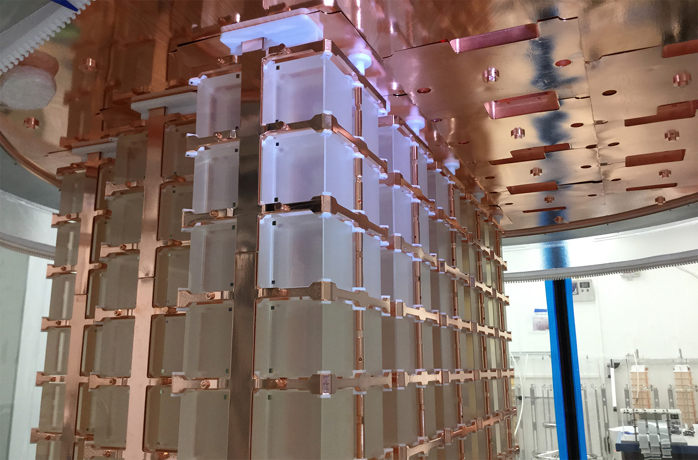 Several towers of translucent cubic detectors in copper frames suspended from a circular plate. One section of crystals appears whiter, almost frosted.