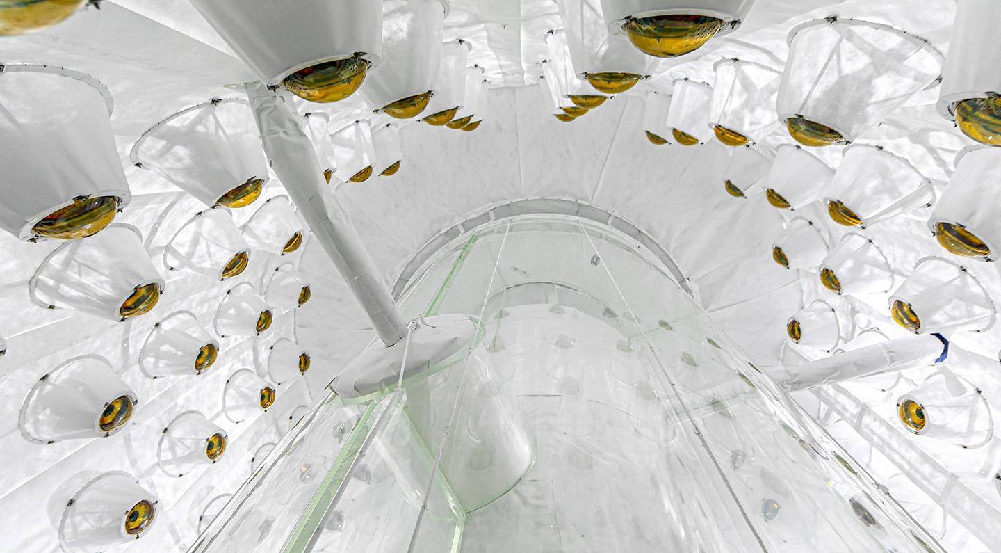 Interior view of the LZ outer detector featuring a bright white cylindrical structure with circular yellow and amber lenses pointed toward the center.