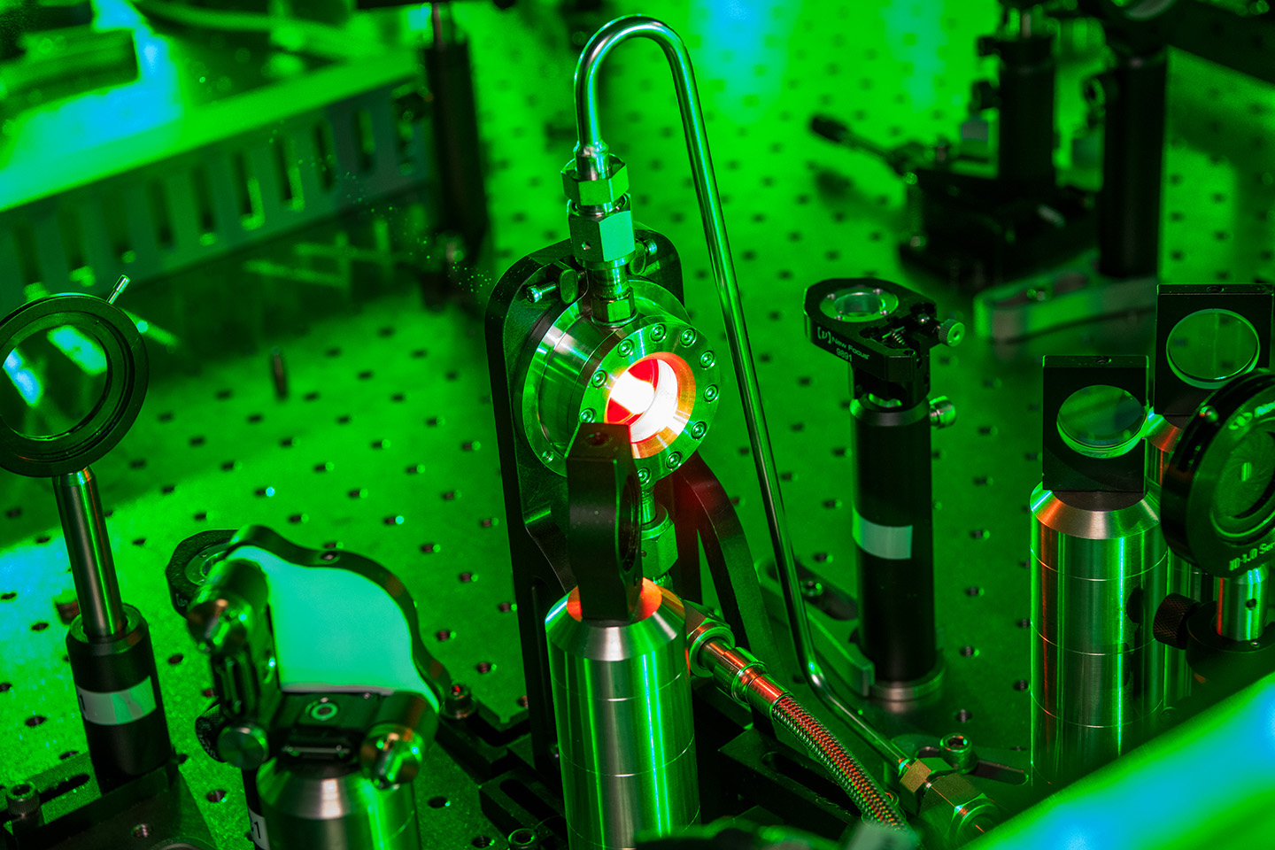 Close-up of laser optics illuminated with green light. The interior of the central cylinder glows red, with its center bright white.