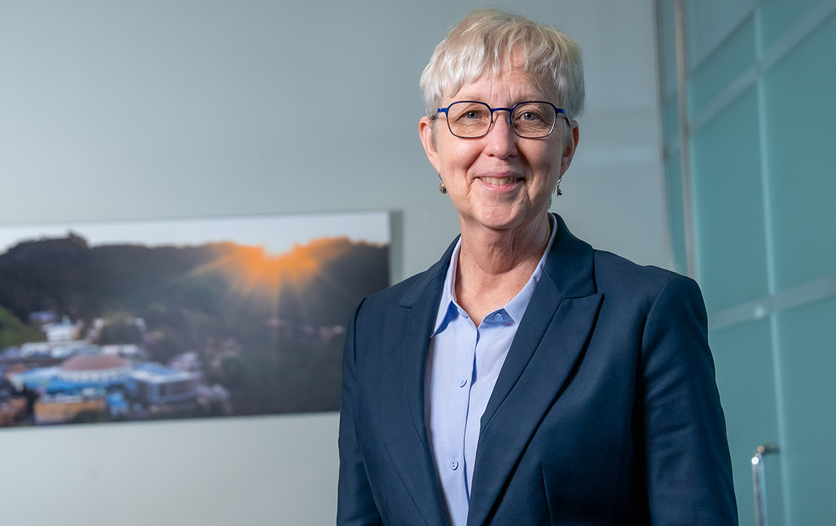 Katherine Yelick standing in front of an aerial image of Berkeley Lab.