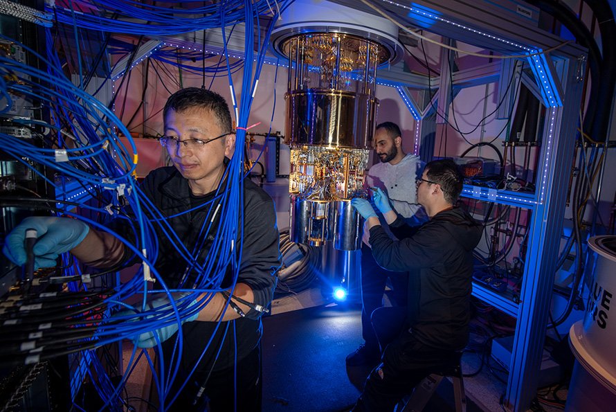 Researchers adjusting controls of a complex blue and copper-colored device.