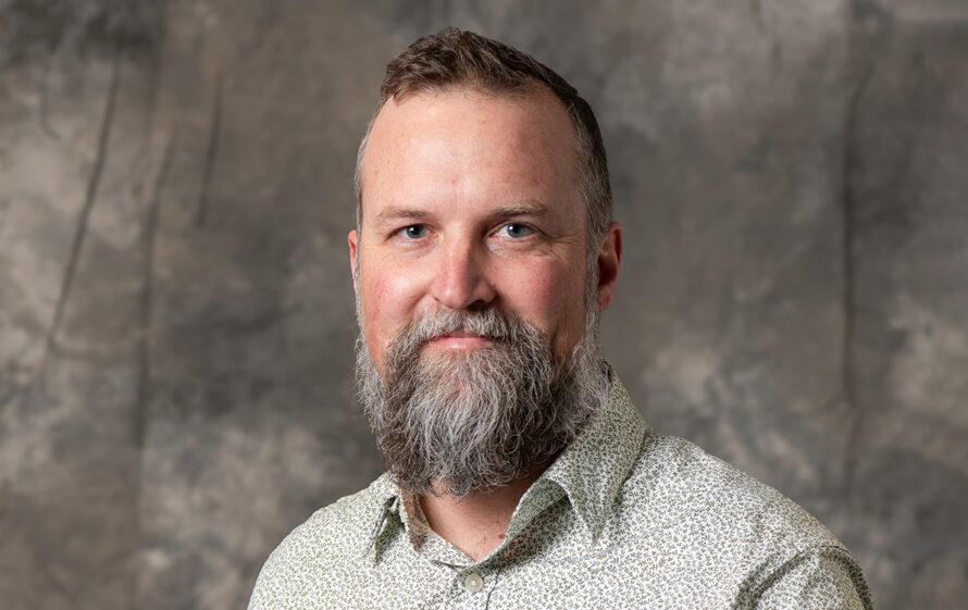 Researcher in a white button-down shirt posing against a gray background.