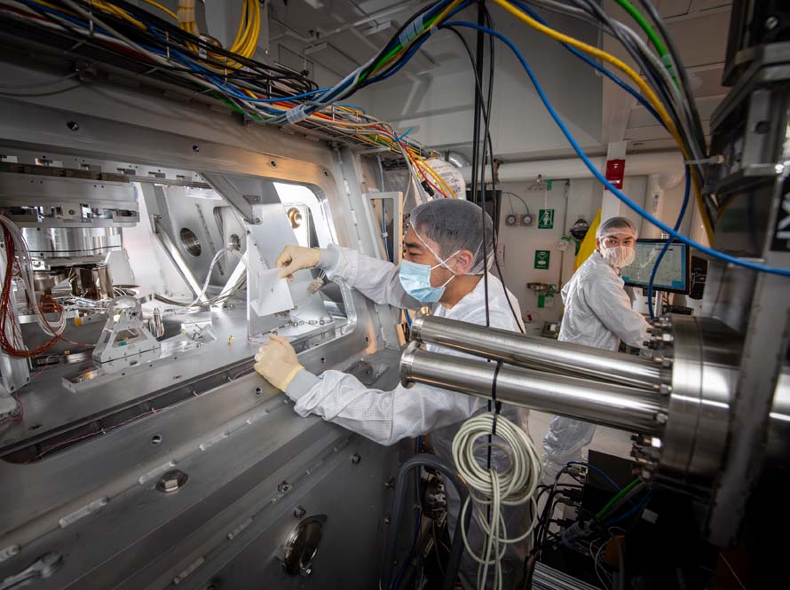 Two researchers wearing white lab coats in a lab with large metal machinery and blue cables.