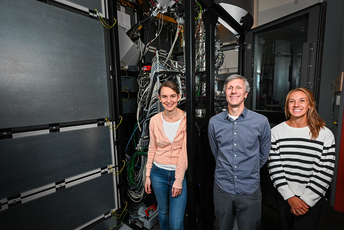 Three researchers in front of a transmission electron microcope.